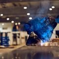Worker welding metal in a factory workshop, surrounded by sparks and blue smoke.
